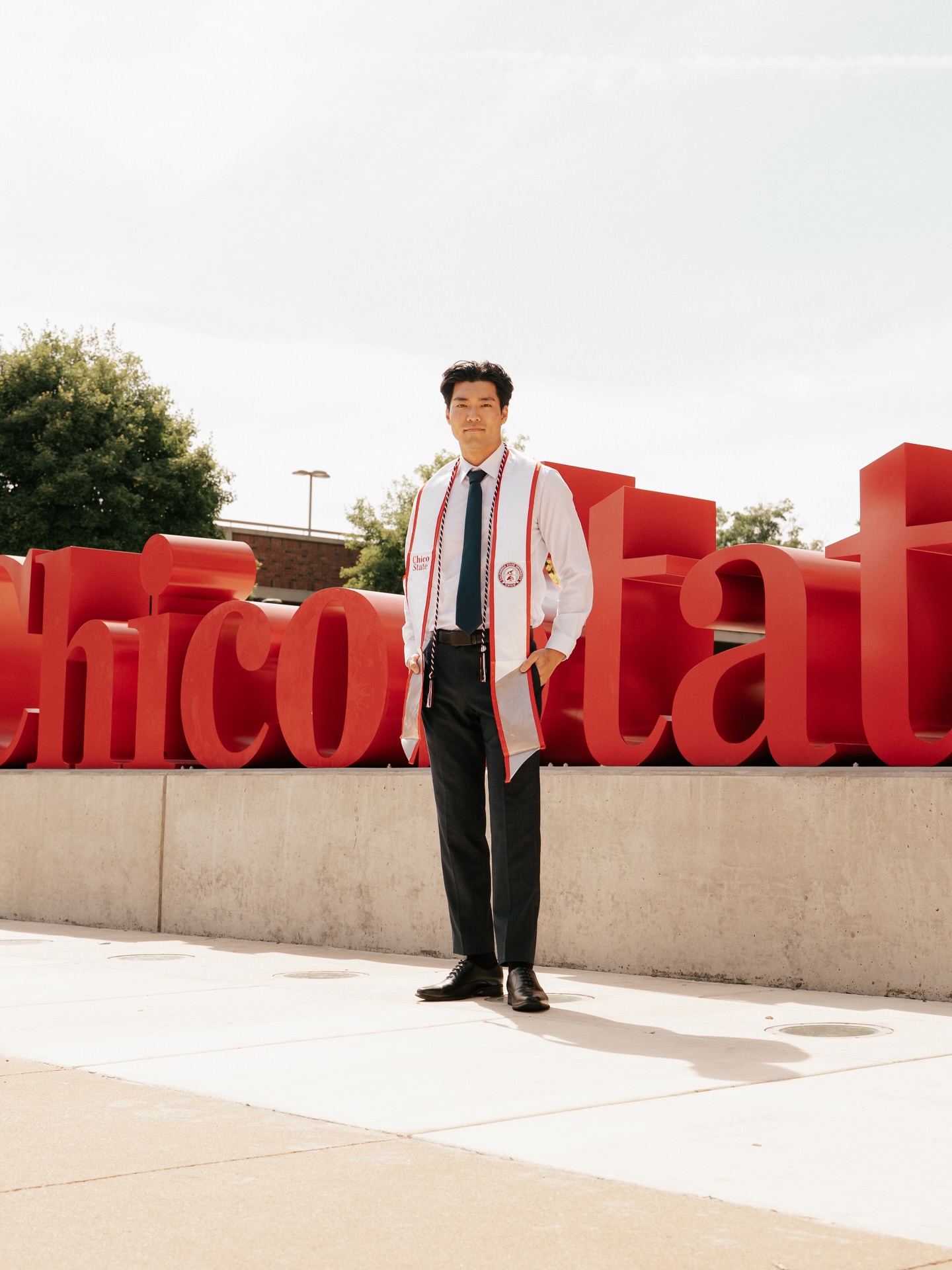 Graduate standing in front of the giant red Chico State letters under a pale sky