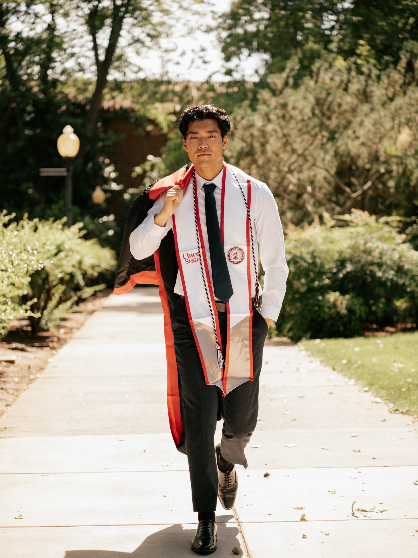 Graduate walking down a sunny campus path, stole swinging