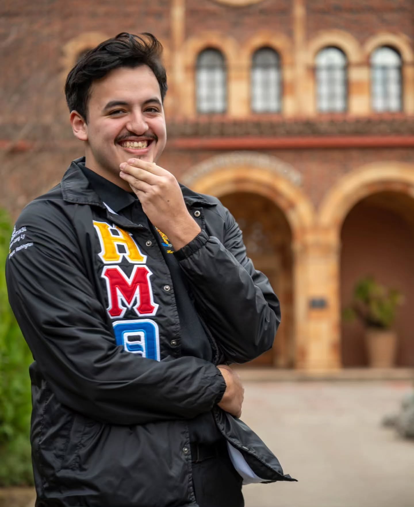 Chapter member laughing with a hand on the chin in front of a brick building