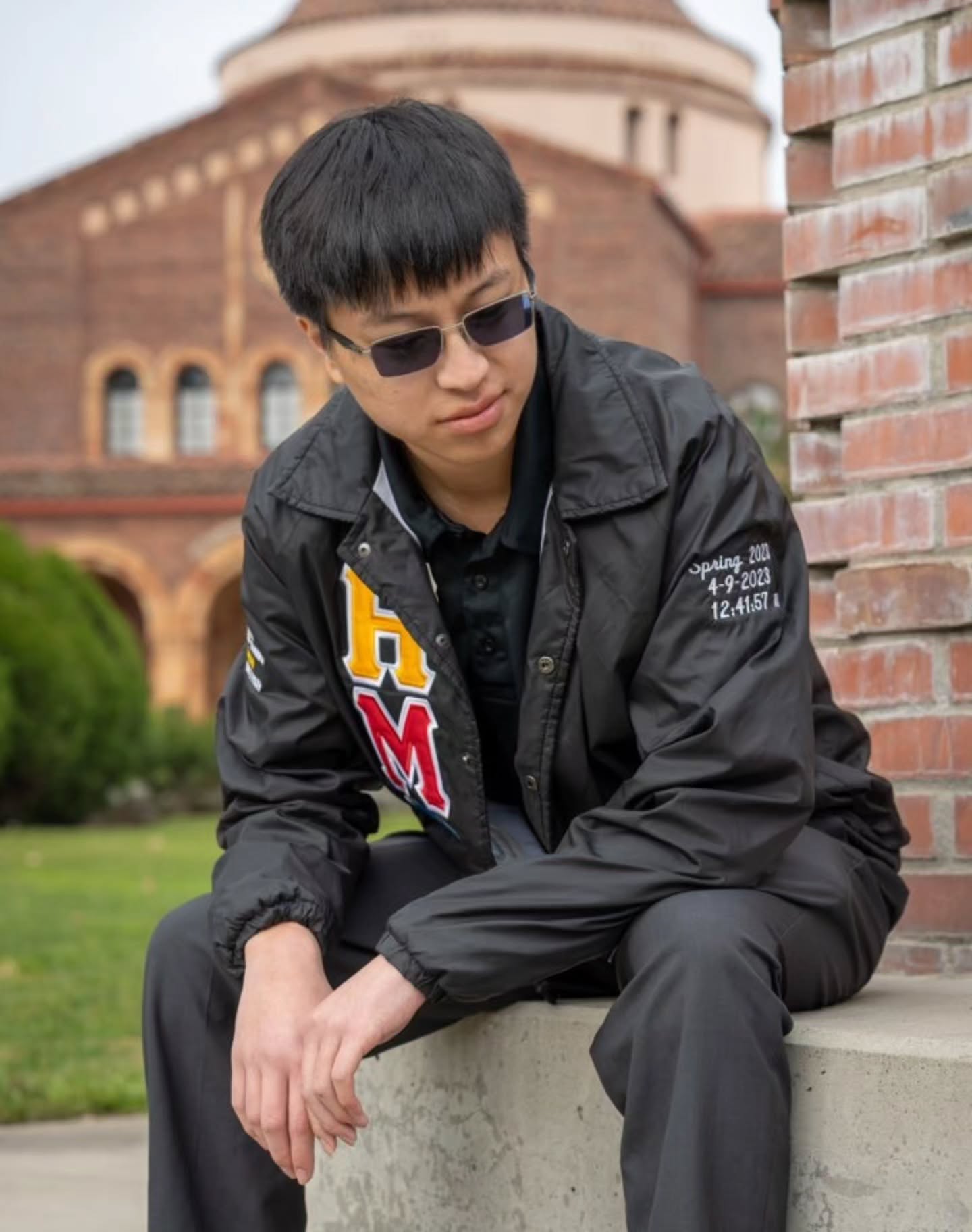 Chapter member in sunglasses sitting on a low wall beside a brick column