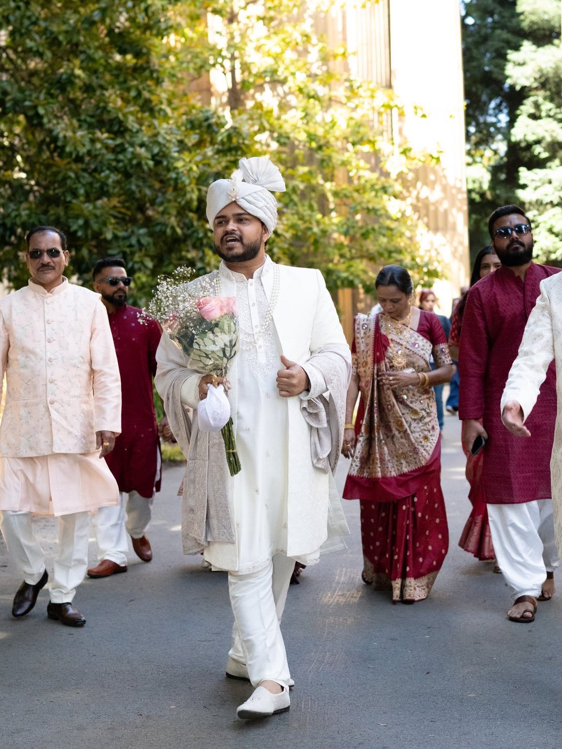 Groom in a white sherwani and turban walking with family during the baraat procession