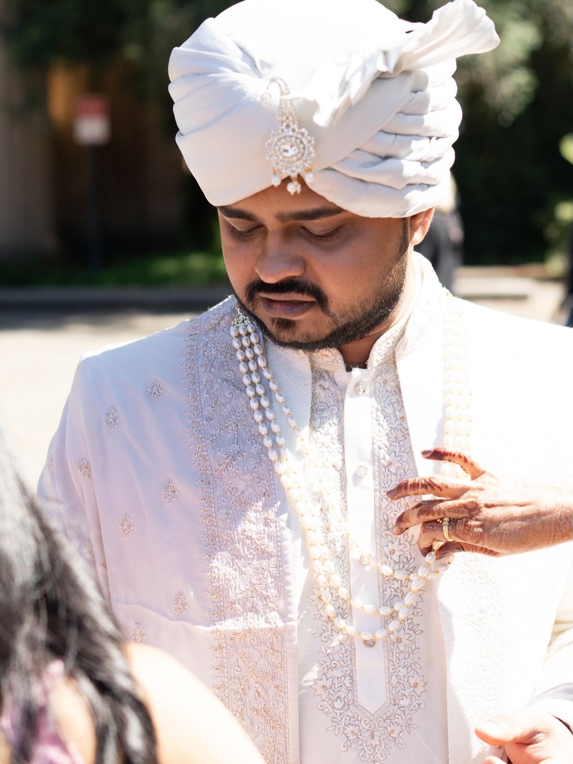 Groom in a white sherwani, pearl necklace and turban looking down