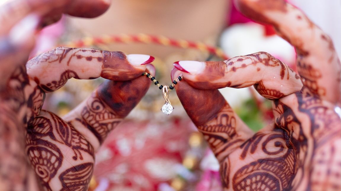 Henna-covered hands holding up a delicate gold pendant necklace