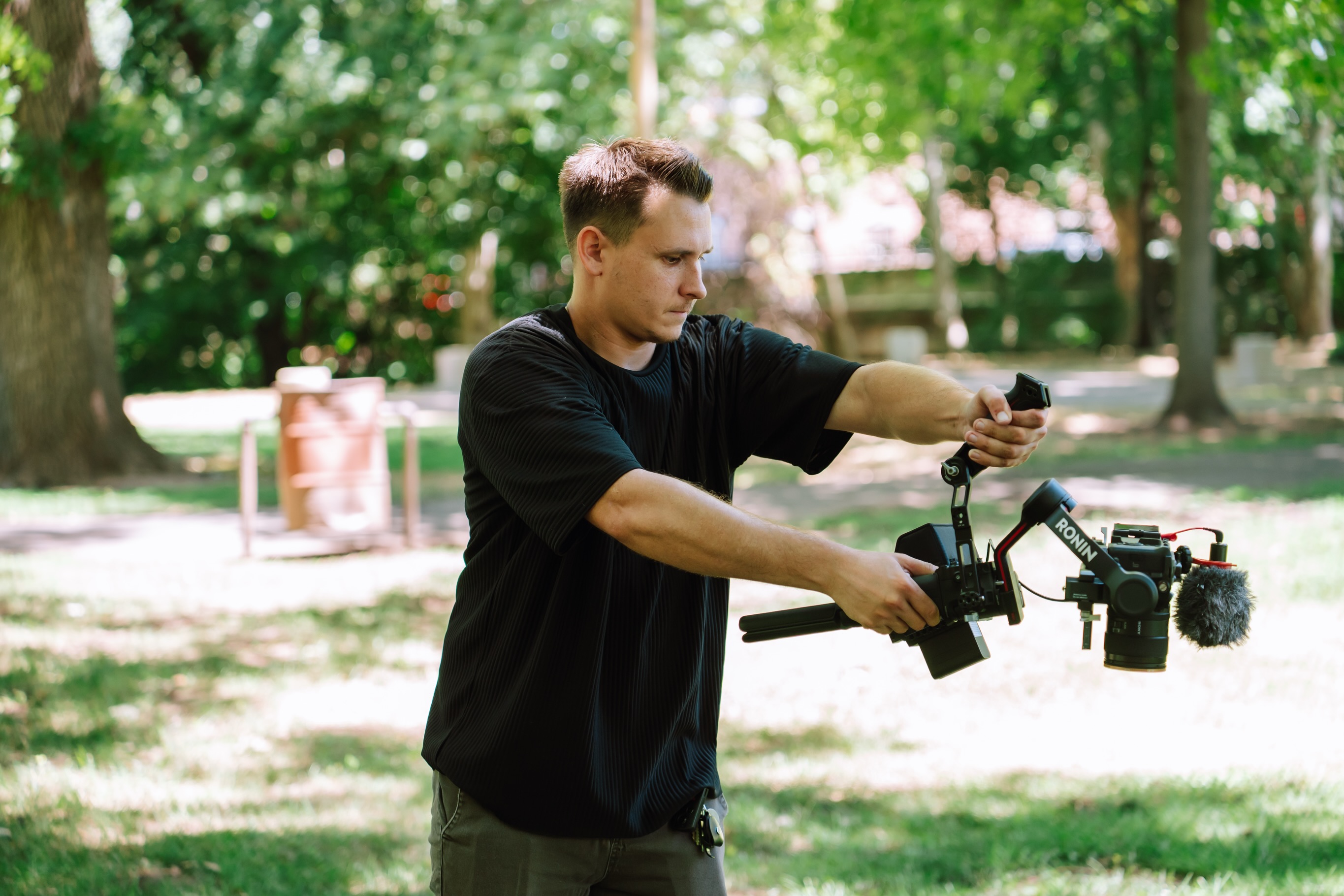 Videographer holding a camera on a gimbal in a shady park